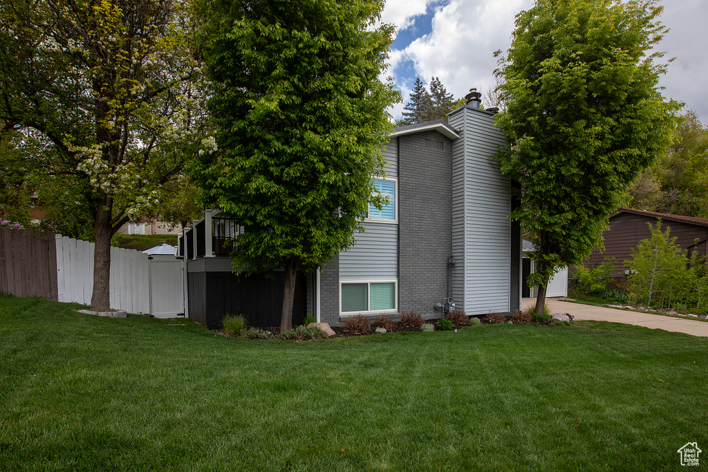 View of side of home with a yard, concrete driveway, fence, and a chimney