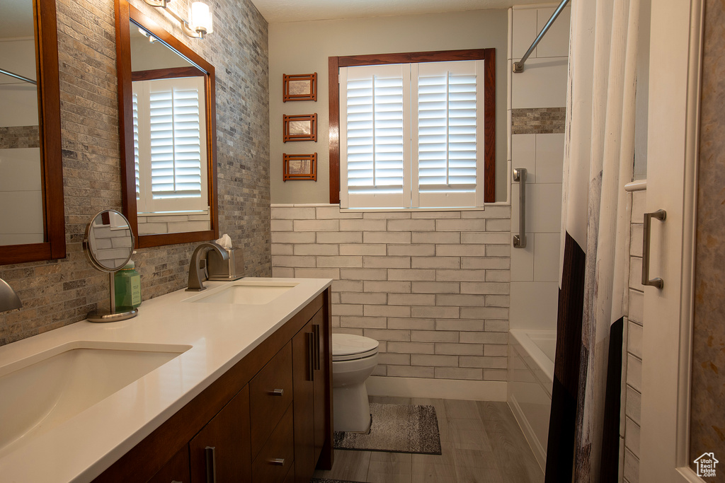 Bathroom with a sink, tile walls, shower / bathtub combination with curtain, and toilet