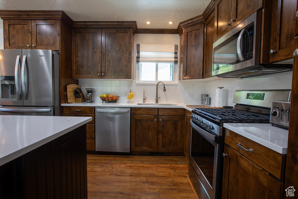 Kitchen featuring decorative backsplash, light countertops, a sink, dark wood finished floors, and appliances with stainless steel finishes
