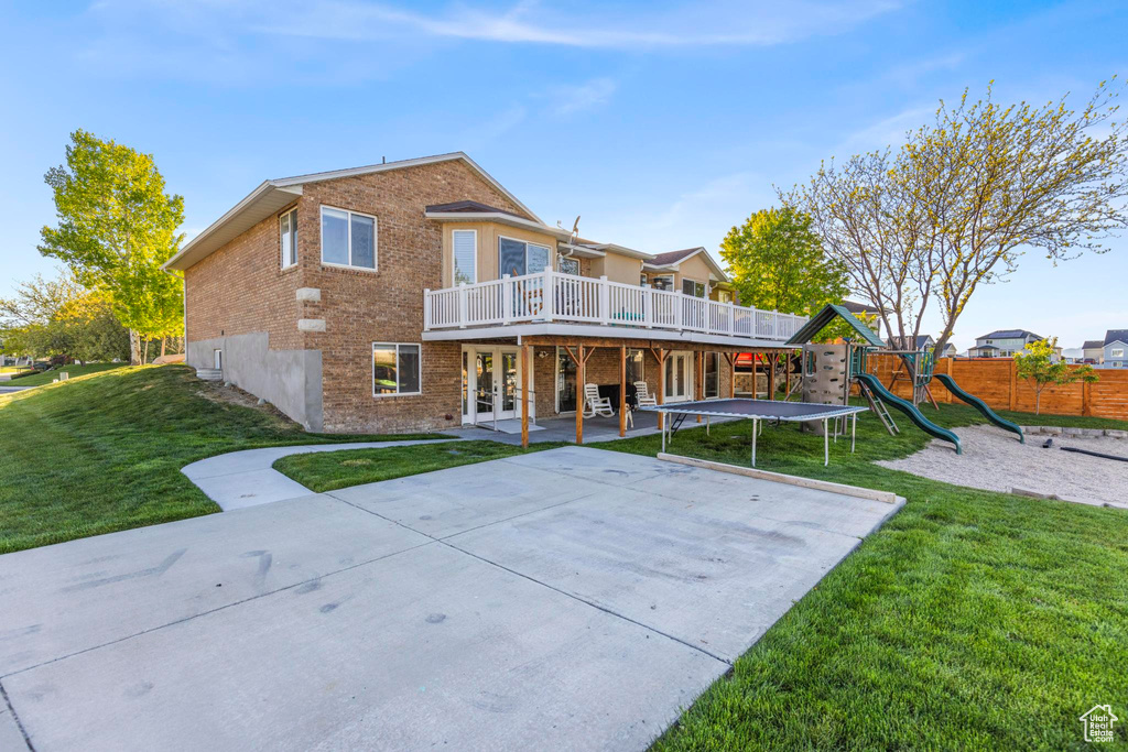 Back of property with brick siding, a deck, a patio area, french doors, and a yard