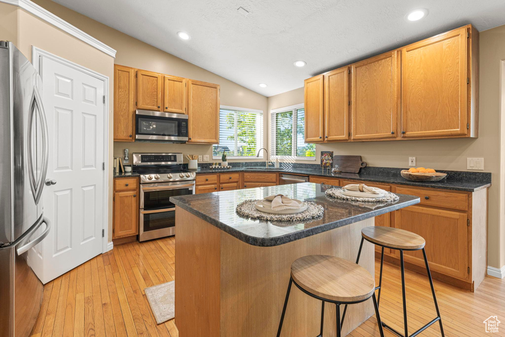 Kitchen with stainless steel appliances, vaulted ceiling, light wood finished floors, and a kitchen bar