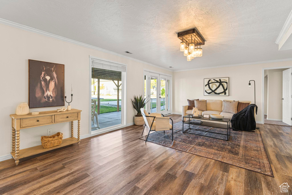 Living room featuring ornamental molding, wood finished floors, baseboards, a textured ceiling, and a notable chandelier