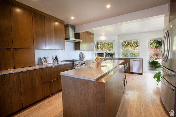 Kitchen with wall chimney range hood, modern cabinets, stainless steel appliances, and light wood finished floors