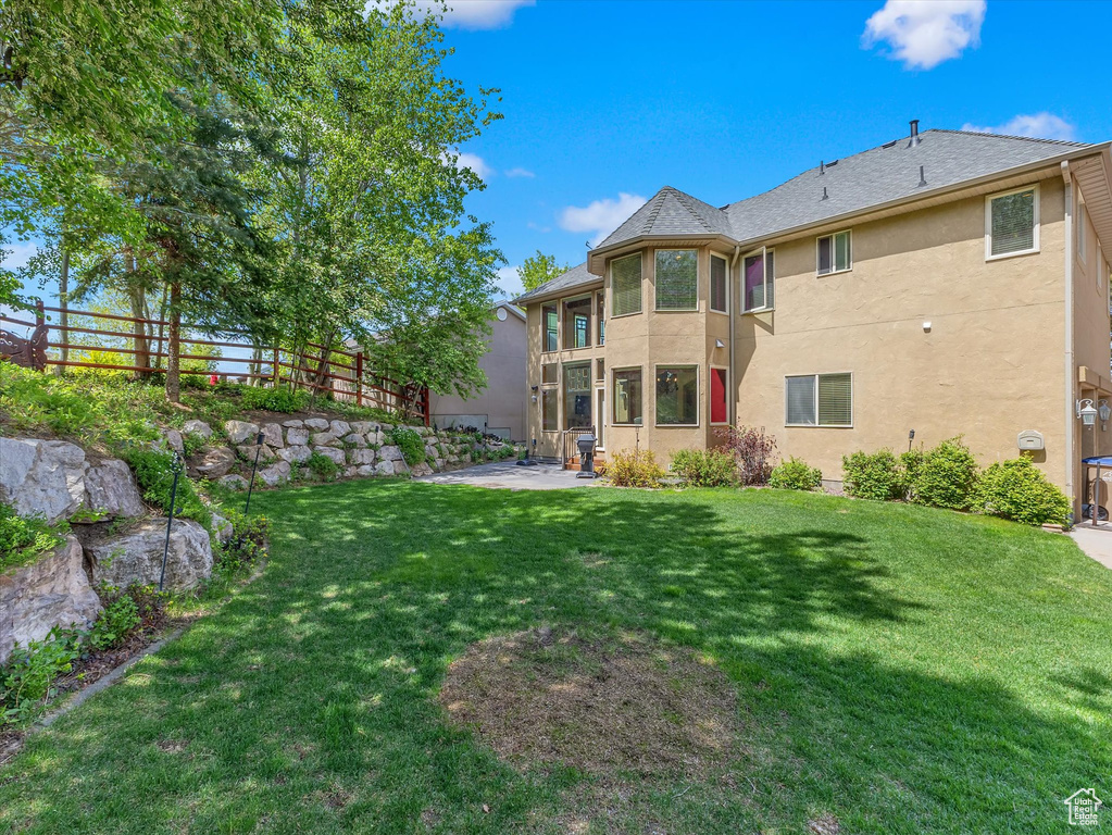 Rear view of property featuring a shingled roof, stucco siding, a fenced backyard, a lawn, and a patio