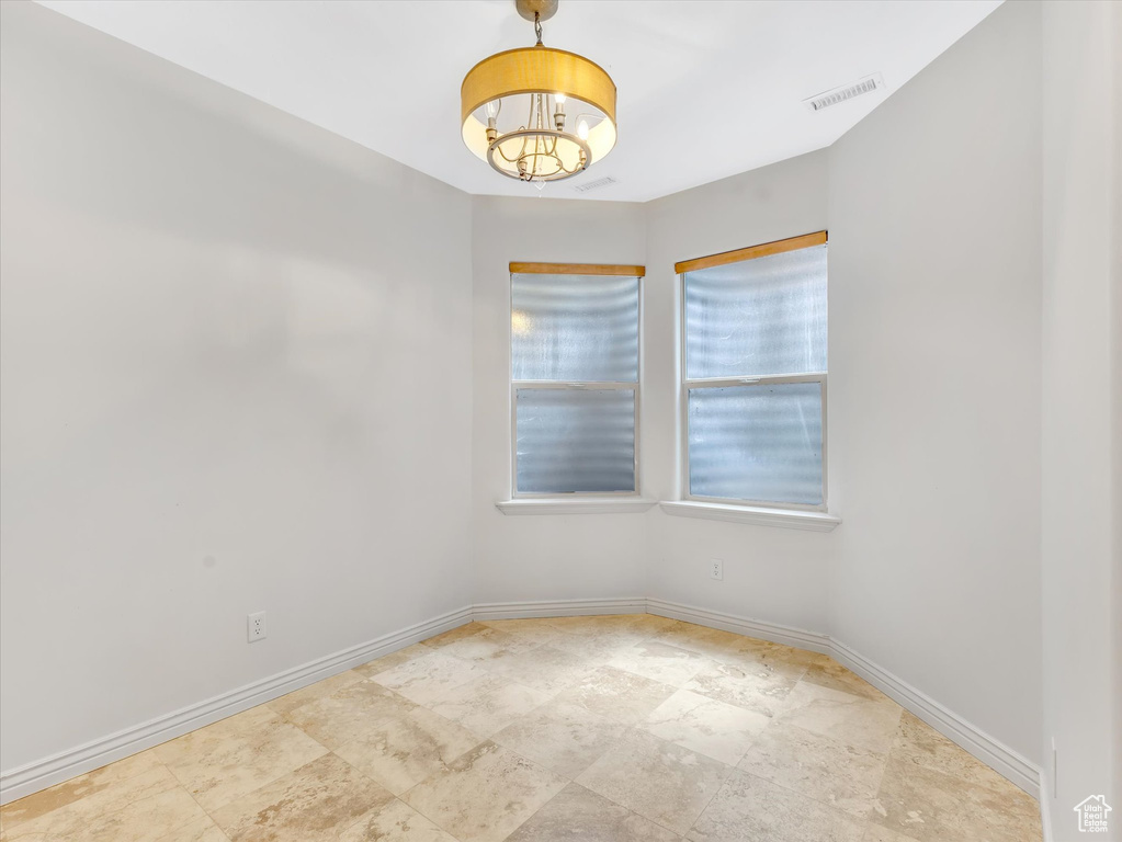 Empty room featuring stone finish floor, baseboards, visible vents, and an inviting chandelier