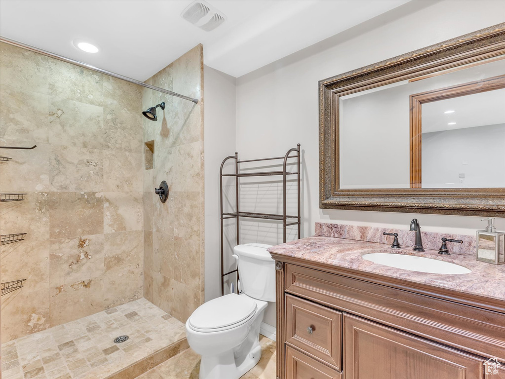 Bathroom featuring toilet, recessed lighting, tiled shower, and vanity