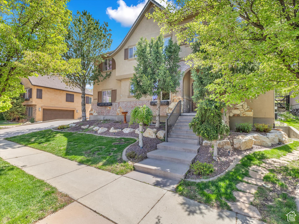 View of front of house featuring a garage, stone siding, a front yard, stucco siding, and driveway