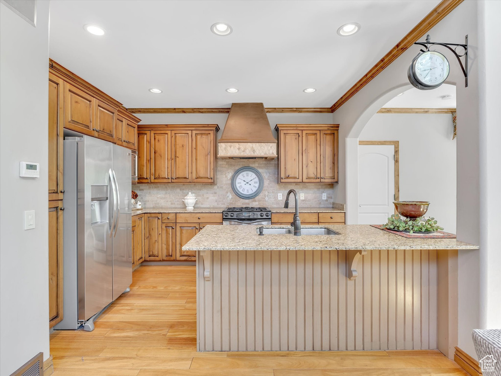 Kitchen featuring crown molding, light stone countertops, a sink, custom exhaust hood, and stainless steel appliances