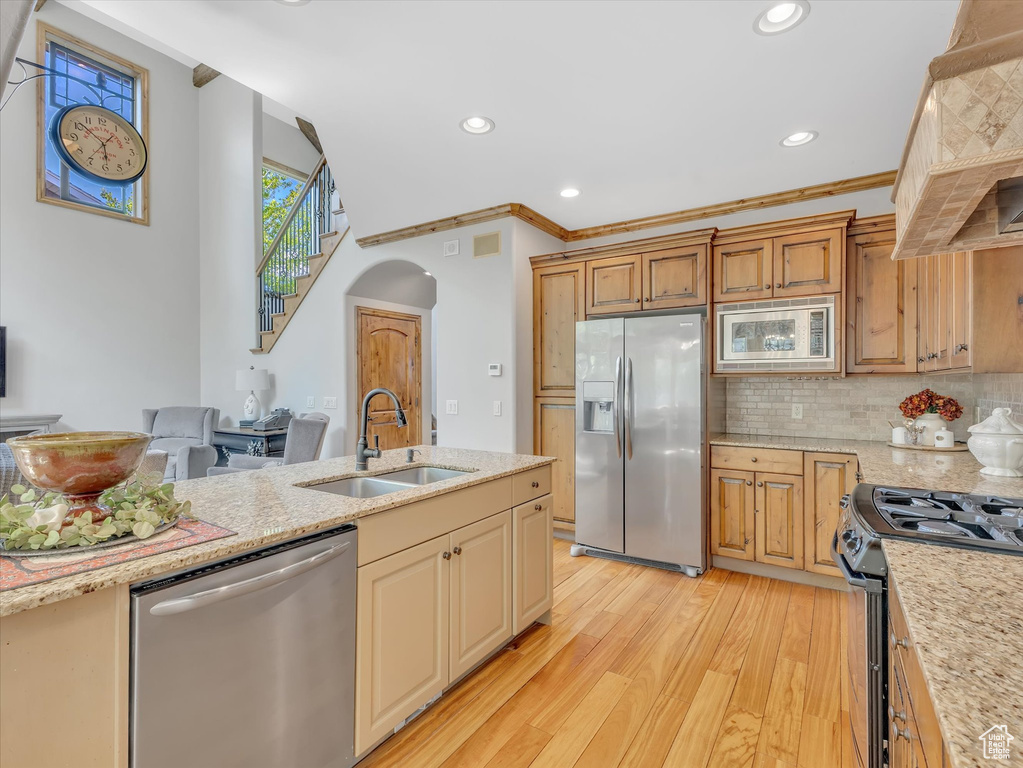 Kitchen with light wood-style floors, arched walkways, custom range hood, a sink, and appliances with stainless steel finishes