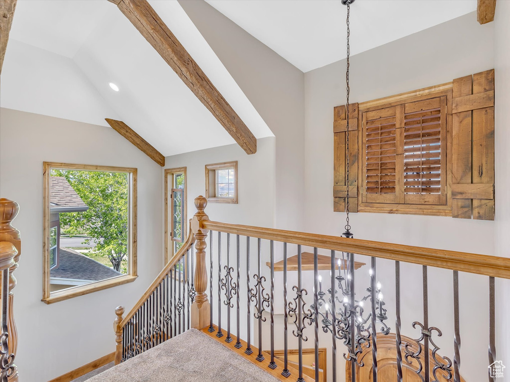 Corridor featuring a healthy amount of sunlight, baseboards, an inviting chandelier, and lofted ceiling with beams