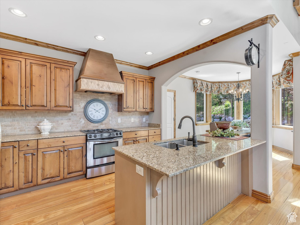 Kitchen featuring light stone countertops, light wood-style floors, premium range hood, stainless steel gas range, and a sink
