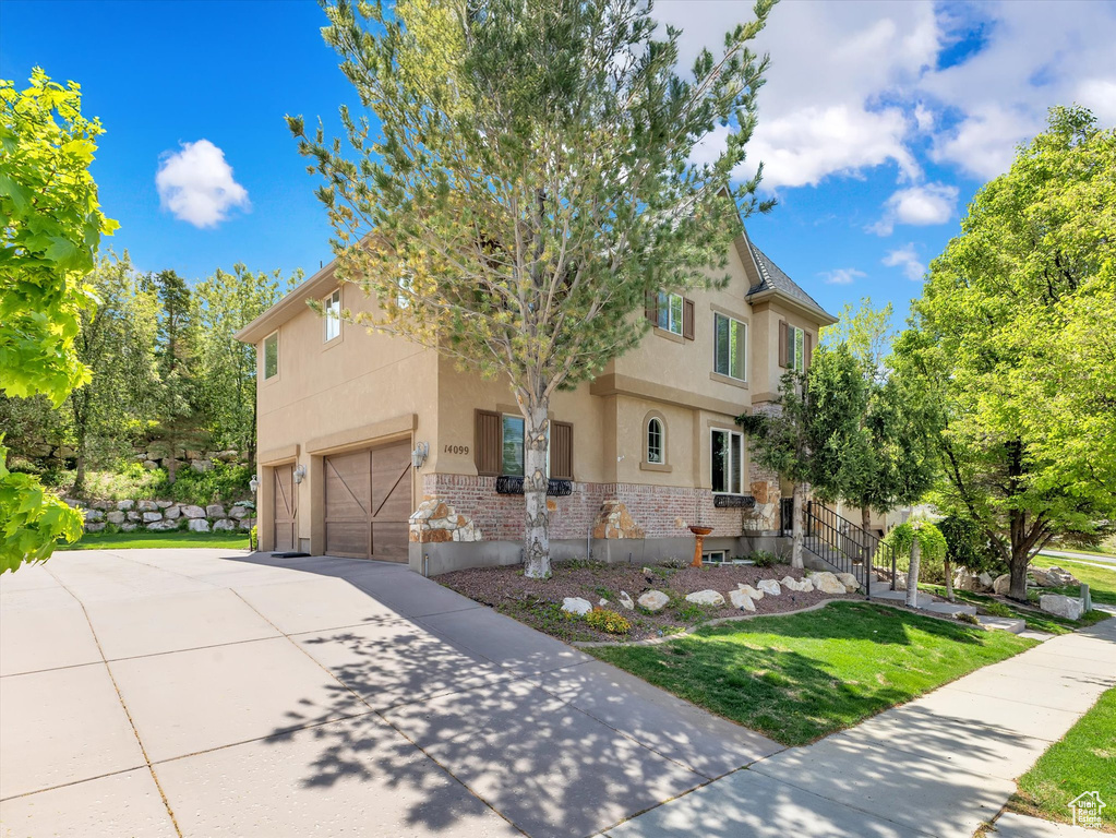 View of front facade featuring an attached garage, a front lawn, brick siding, stucco siding, and driveway