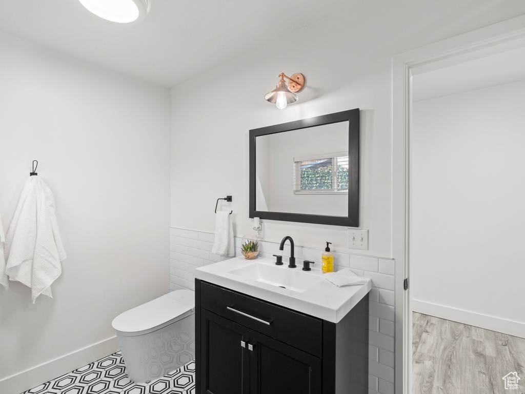 Half bath featuring baseboards, vanity, toilet, and tile walls