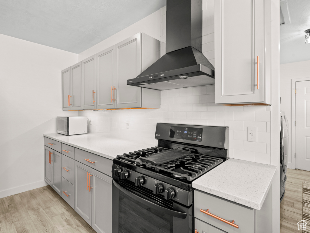 Kitchen with backsplash, range with gas stovetop, light wood-style flooring, and wall chimney exhaust hood