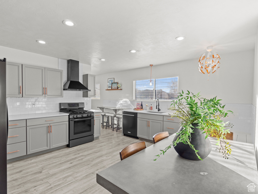 Kitchen with a sink, dishwasher, wall chimney exhaust hood, gas range, and gray cabinetry
