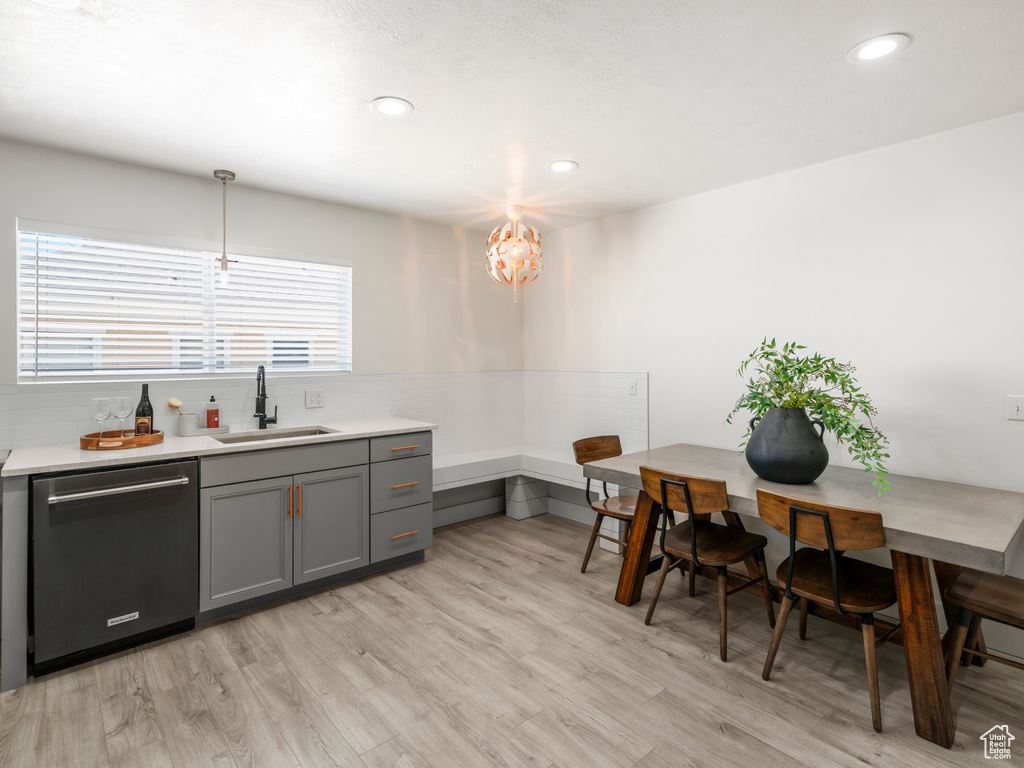 Kitchen with light wood-style floors, dishwashing machine, light countertops, a sink, and gray cabinetry