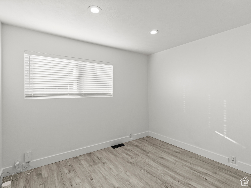 Empty room with light wood-style floors, baseboards, recessed lighting, and visible vents