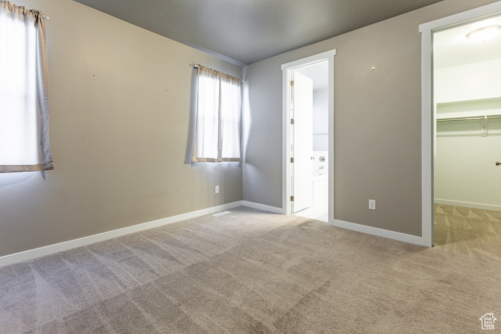 Unfurnished bedroom featuring a walk in closet, baseboards, a closet, connected bathroom, and carpet