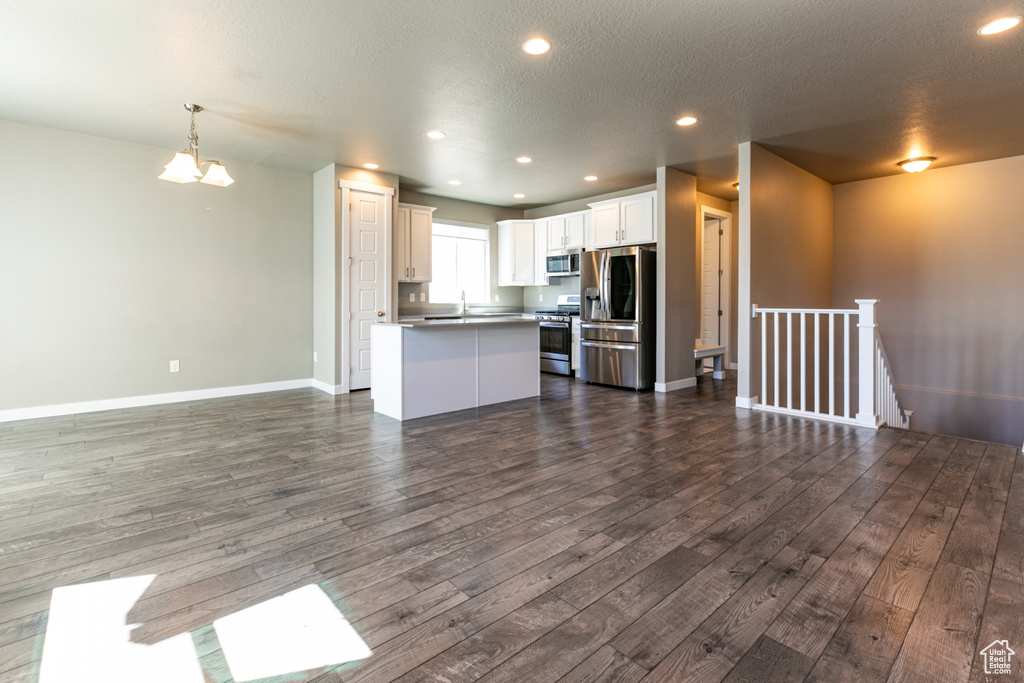 Unfurnished living room featuring dark wood-type flooring, recessed lighting, baseboards, and an inviting chandelier