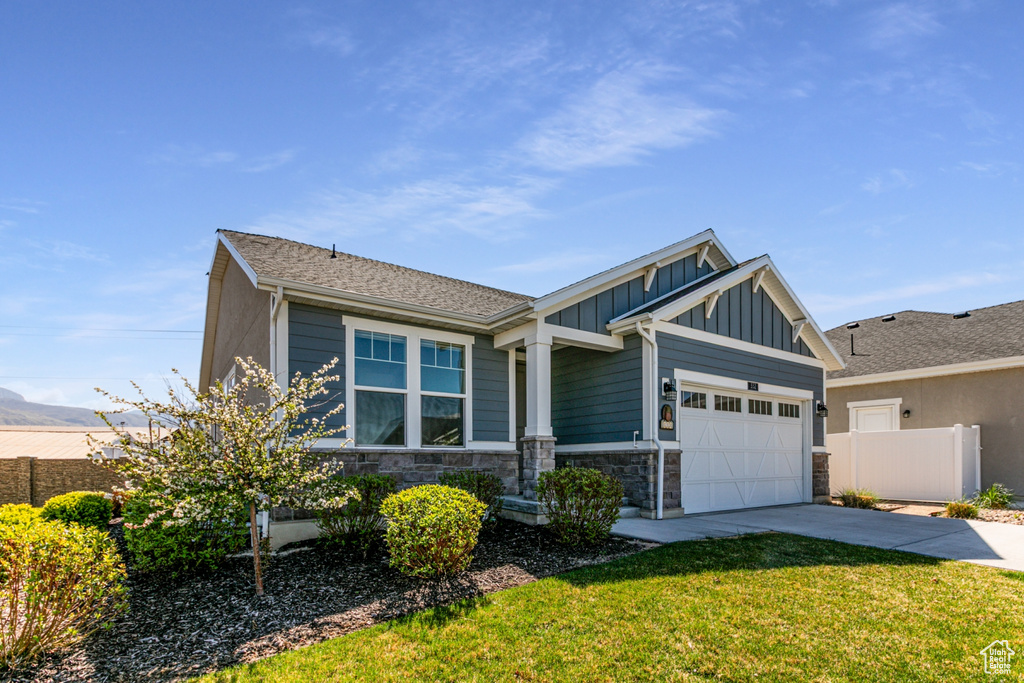 Craftsman-style house with board and batten siding, driveway, a garage, fence, and stone siding