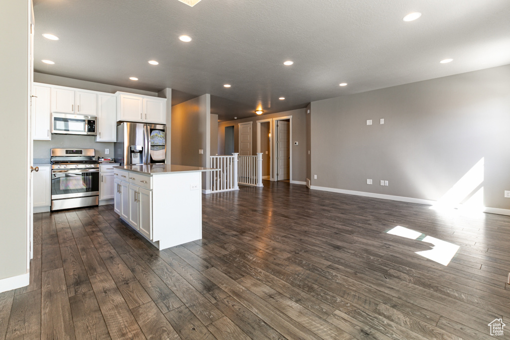 Kitchen with appliances with stainless steel finishes, white cabinetry, open floor plan, dark wood-type flooring, and a kitchen island