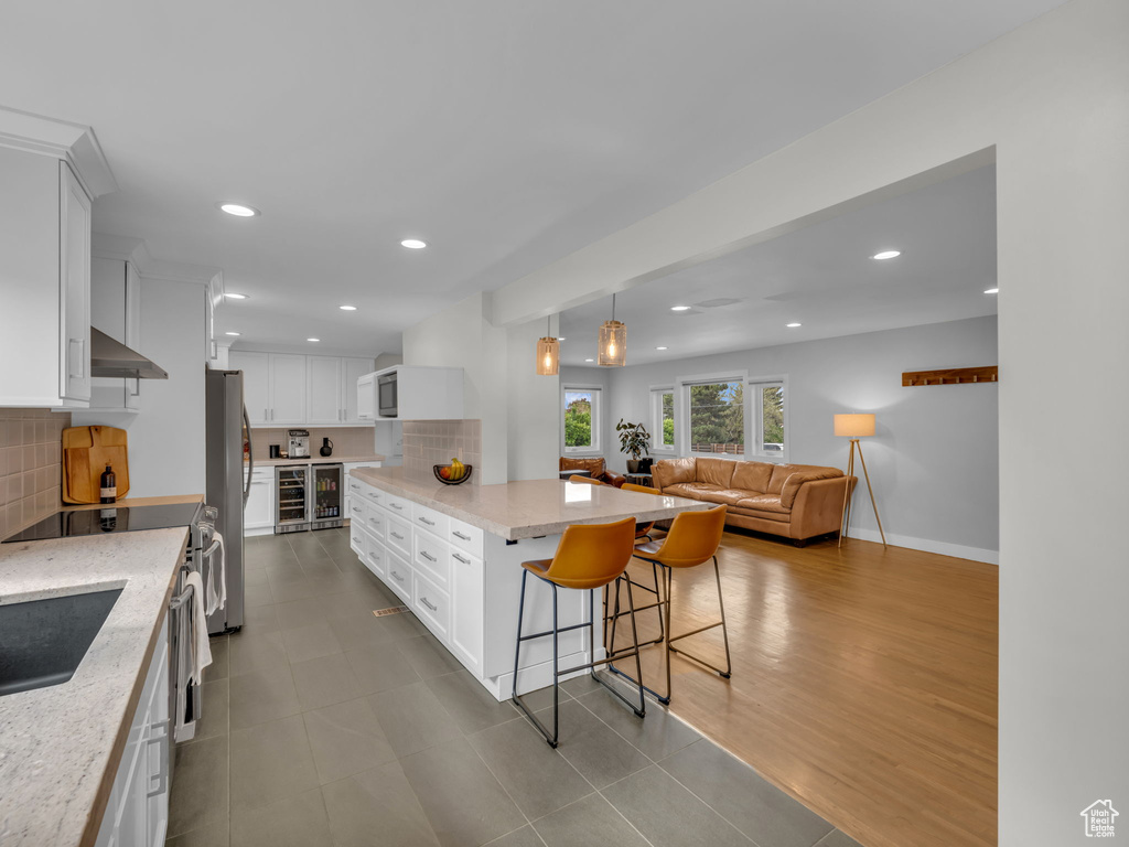 Kitchen featuring appliances with stainless steel finishes, exhaust hood, decorative backsplash, and beverage cooler