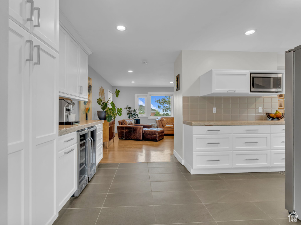 Kitchen with decorative backsplash, beverage cooler, light countertops, white cabinetry, and stainless steel appliances
