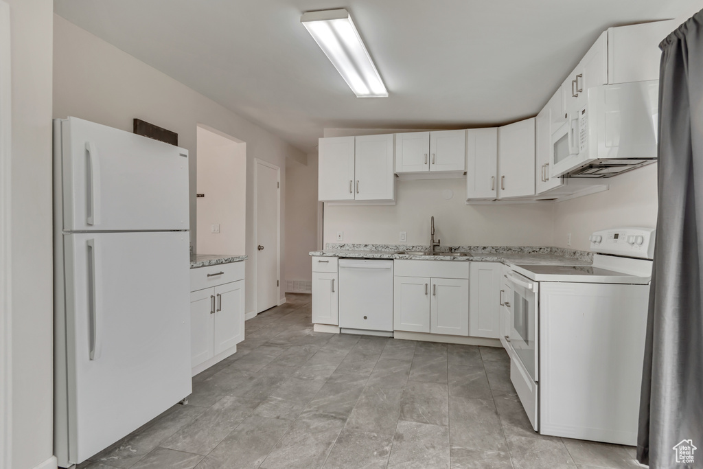 Kitchen with light stone counters, a sink, white cabinets, and white appliances