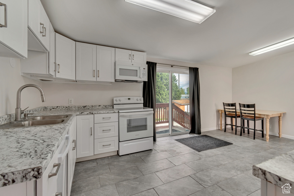 Kitchen featuring white appliances, white cabinets, light stone countertops, and a sink