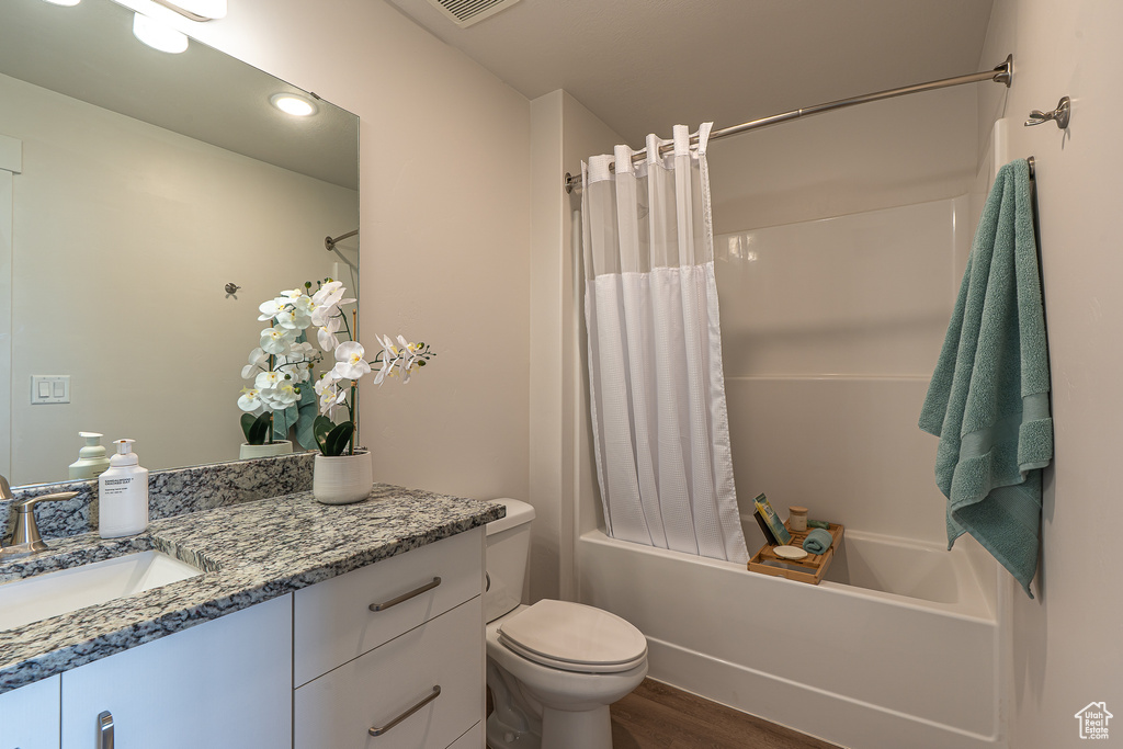 Full bathroom featuring wood finished floors, vanity, toilet, shower / tub combo with curtain, and recessed lighting