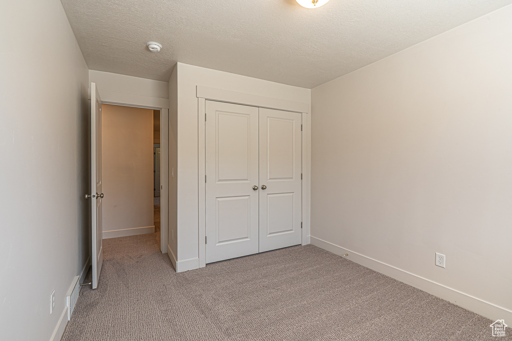Unfurnished bedroom featuring baseboards, a closet, a textured ceiling, and light colored carpet