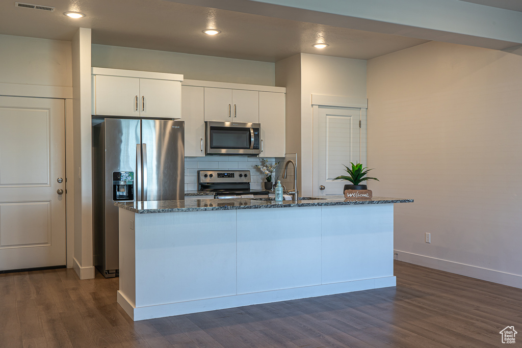 Kitchen with dark wood-type flooring, dark stone counters, tasteful backsplash, a sink, and stainless steel appliances