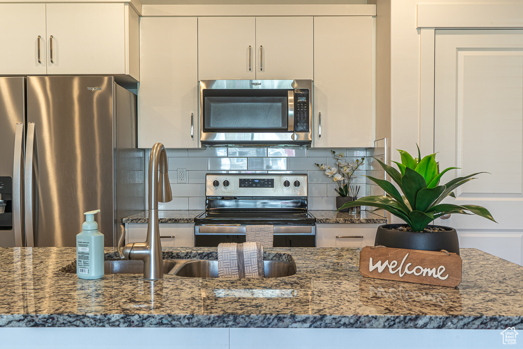 Kitchen with decorative backsplash, dark stone countertops, white cabinets, and stainless steel appliances