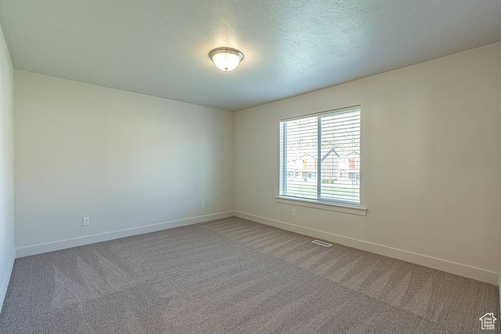 Spare room featuring carpet flooring, a textured ceiling, baseboards, and visible vents