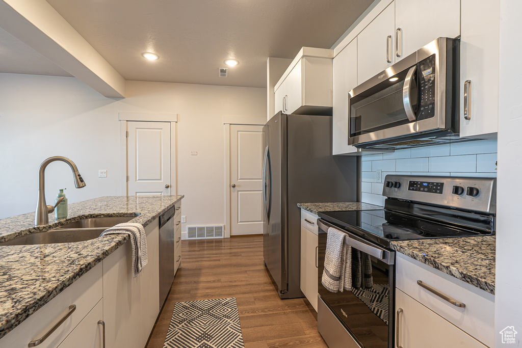 Kitchen featuring appliances with stainless steel finishes, a sink, white cabinetry, tasteful backsplash, and visible vents