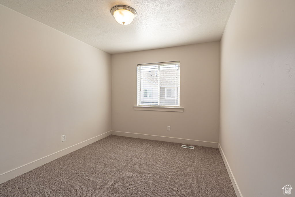 Empty room featuring carpet flooring, a textured ceiling, visible vents, and baseboards