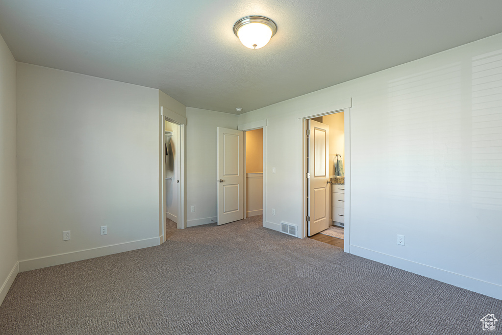 Unfurnished bedroom featuring visible vents, baseboards, ensuite bathroom, and light colored carpet