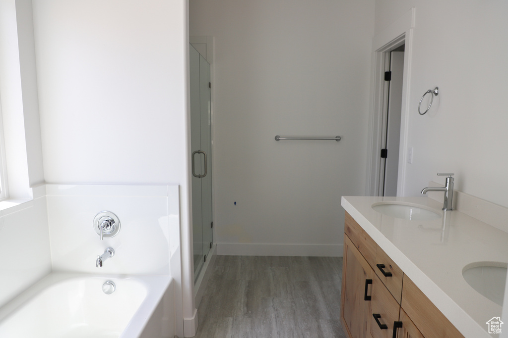 Bathroom with double vanity, a bath, a stall shower, wood finished floors, and a sink
