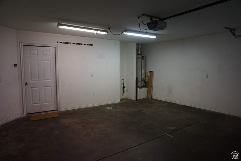 Garage with gas water heater, a garage door opener, and baseboards