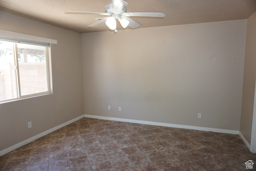 Empty room featuring a textured ceiling, ceiling fan, and baseboards