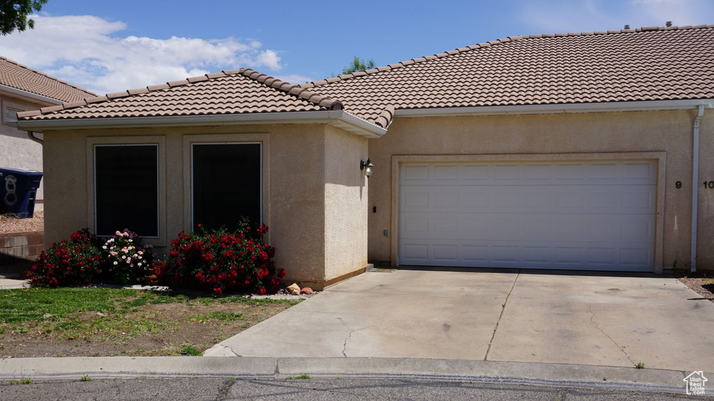 View of front of property featuring concrete driveway, a garage, a tile roof, and stucco siding