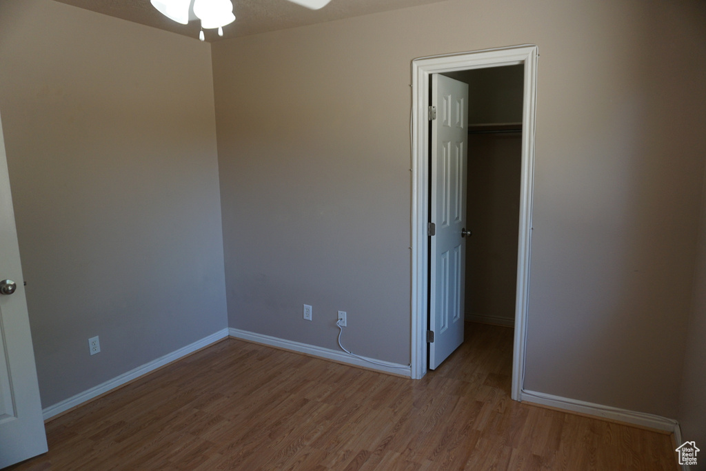 Unfurnished bedroom with wood finished floors, a spacious closet, baseboards, and a closet