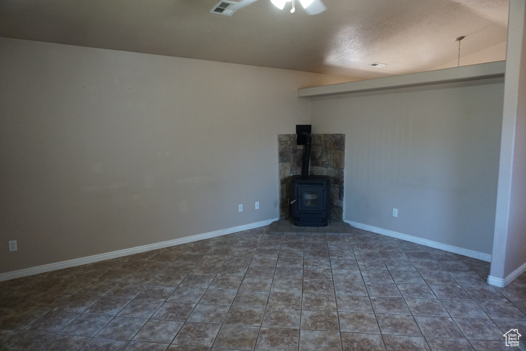 Unfurnished living room featuring ceiling fan, tile patterned flooring, a wood stove, and baseboards