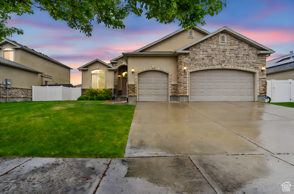 View of front facade featuring a front yard, fence, concrete driveway, an attached garage, and stone siding
