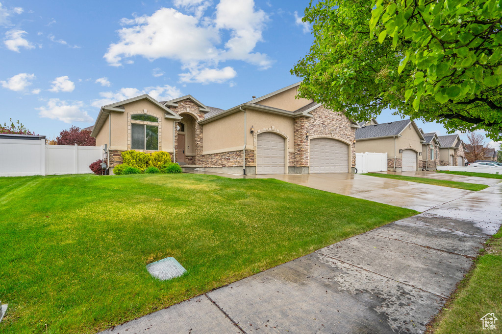 View of front of property with fence, a front lawn, concrete driveway, stone siding, and stucco siding