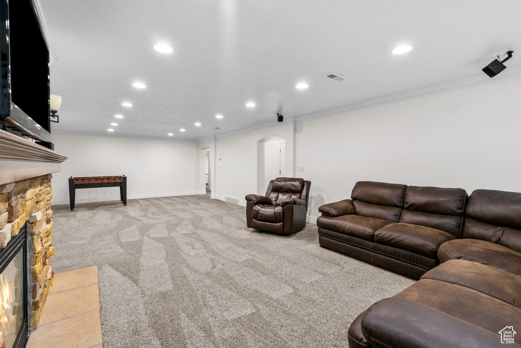 Living area with crown molding, visible vents, a stone fireplace, recessed lighting, and light colored carpet