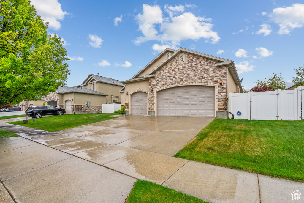 View of front of property with an attached garage, driveway, a front lawn, and stone siding