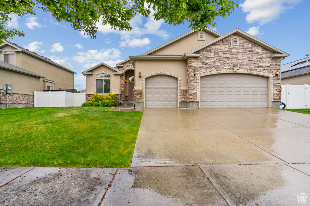 View of front of home featuring stone siding, a front yard, stucco siding, an attached garage, and driveway