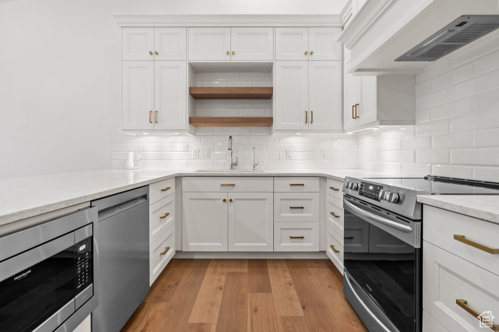 Kitchen featuring decorative backsplash, light wood-type flooring, custom range hood, a sink, and appliances with stainless steel finishes