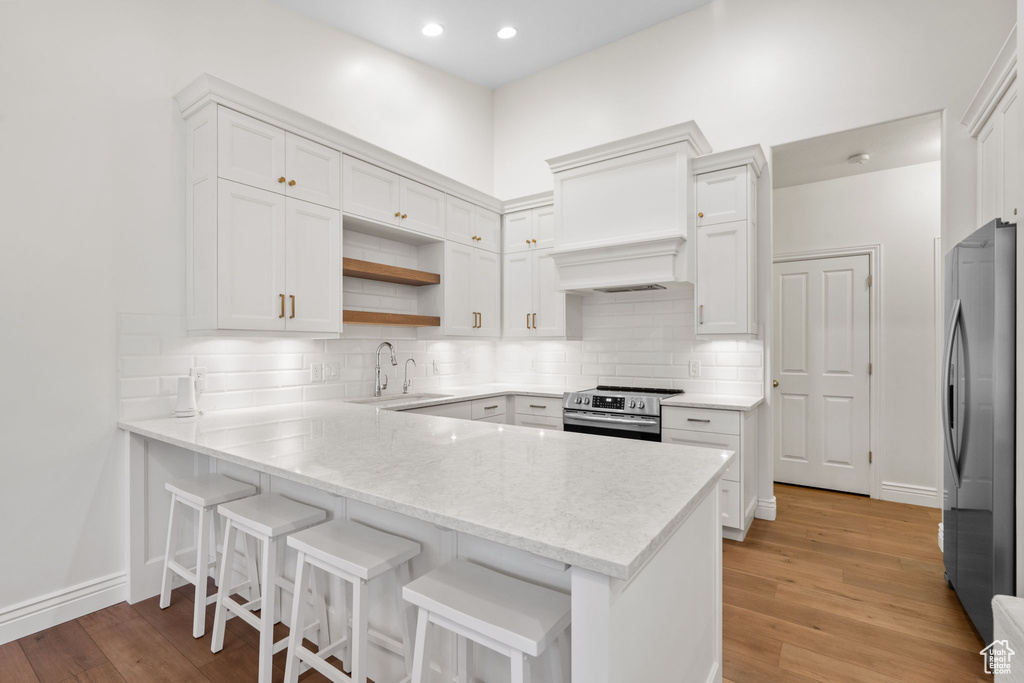 Kitchen with appliances with stainless steel finishes, light wood-type flooring, a sink, white cabinets, and a peninsula
